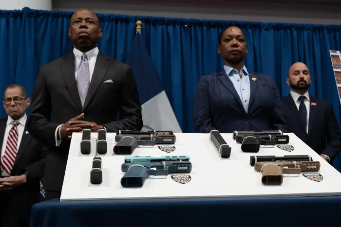 Mayor Eric Adams and Police Commissioner Keechant Sewell standing behind a board showing four guns laying flat